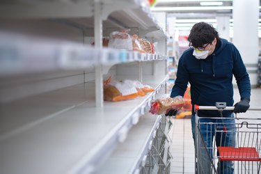 Man's hands in protective gloves searching bread on empty shelves in a groceries store