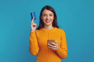 Girl holding smartphone and plastic credit card isolated over blue background