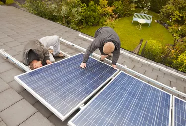 Technicians fitting solar photo voltaic panels to a house roof in Ambleside, Cumbria, UK.