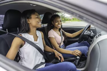 Young black teenage driver seated in her new car with her mother