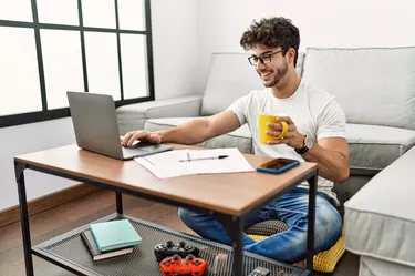 Young hispanic man using laptop and drinking coffee at home