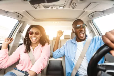 Happy black couple in sunglasses enjoying music driving luxury car