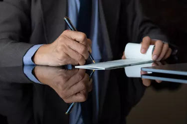 Businessman in suit hand signs cheque. Paycheck concept.