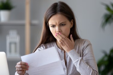 Shocked stressed young woman reading document letter about debt