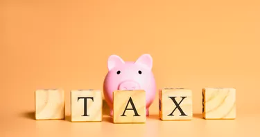 Tax. The word Tax written in English language on wooden cubes. A piggy bank in the image composition. Finance and taxes concepts.