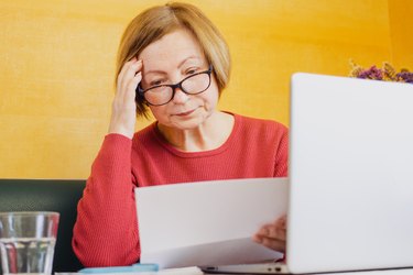 Shocked worried mature woman reading paper document or postal letter feeling frustrated by unexpected news sitting at home indoor. Received bank account balance or bad notice, fine, bankruptcy