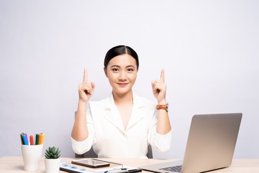 Portrait of businesswoman gesturing while sitting at desk against white background