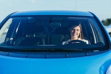 portrait of a successful and happy woman driving a car, photo from the front through the glass