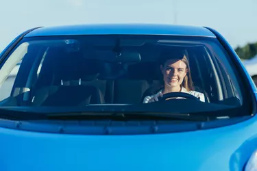portrait of a successful and happy woman driving a car, photo from the front through the glass