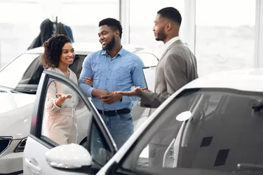 Couple Choosing Car Consulting With Professional Auto Salesman In Dealership