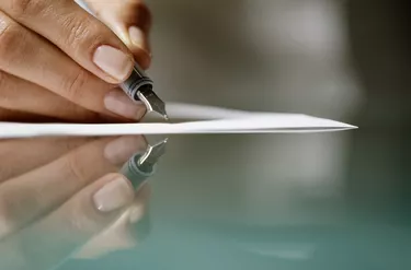 Woman signing on paper, reflected in glass table, close-up