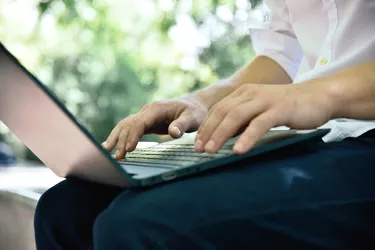 Student sitting in park and typing on laptop.