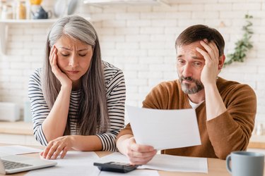 Sad disappointed mature middle-aged couple family wife and husband counting funds, savings, declarations, investments,paperwork, financial documents, bankruptcy, court case, bills, pension at home.