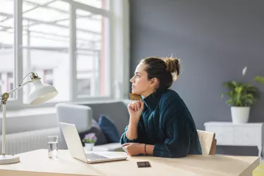 Profile of pensive woman with laptop and credit card sitting at desk at home looking out of window