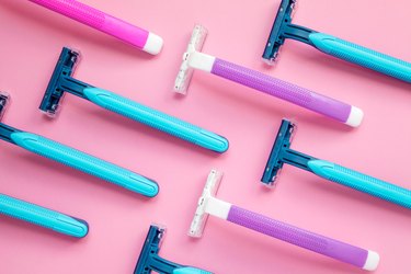 Many disposable purple and blue razors on a pink background