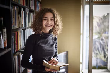 Portrait of a smiling teenage girl holding book at home