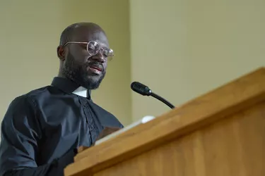 Young priest in black shirt with clerical collar pronouncing speech by pulpit