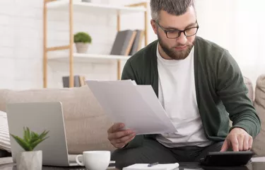 Man with calculator counting money and checking bills at home