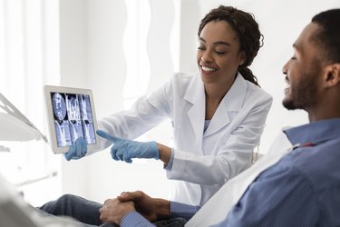Smiling african female dentist showing patient teeth xray