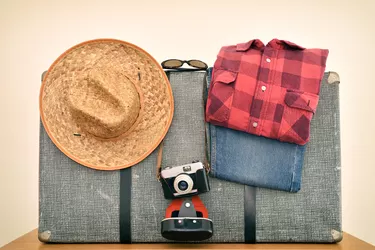 Vintage suitcase with straw hat, travel clothes, sunglasses and photo camera on the wooden table