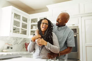 Smiling man embracing female partner in kitchen at home