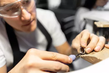 Close-up of silver shavings on ring. Chamfering ring with special tool. Man's hands. Blurred foreground. Male Jewelry Master in goggles.