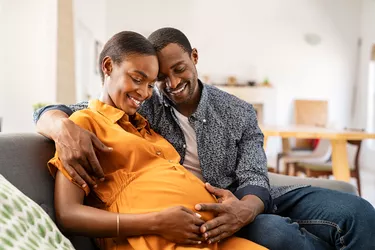 Black expectant parents sitting on sofa dreaming about their baby