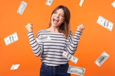 Money rain. Yes I did it! Portrait of joyous winner, young woman in casual shirt standing with clenched fists and closed eyes, celebrating victory and richness.