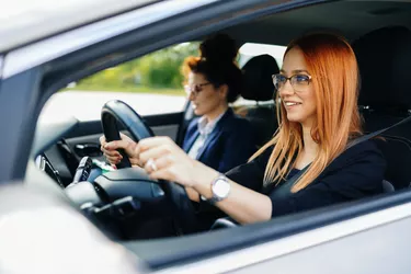 Driving school or test. Beautiful young woman learning how to drive car together with her instructor.