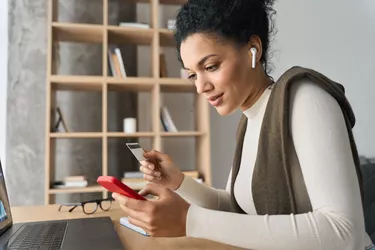 Young adult African american girl sitting indoors doing mobile payment online.