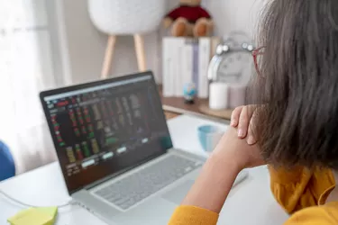 Woman sits at desk while looking online trading screen on laptop