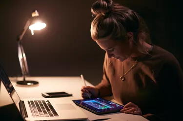 Female Share Trader At Desk With Stock Price Data Displayed On Laptop And Digital Tablet