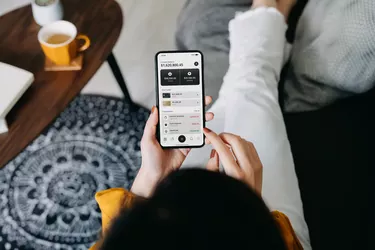 Overhead view of young Asian woman relaxing on the sofa in the living room, managing online banking with smartphone at cozy home. Transferring money, paying bills, checking balances. Technology makes life so much easier