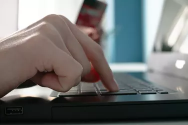 Close up of an unrecognizable person typing while online shopping, with a credit card blurred on the other hand