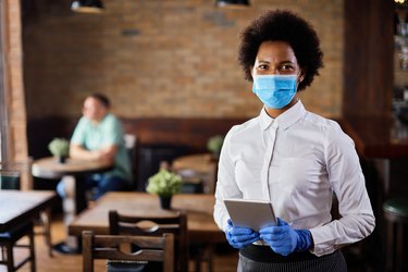 African American waitress wearing protective face mask and gloves while working in cafe.
