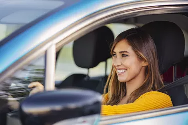 Portrait of happy female driver steering car with safety belt