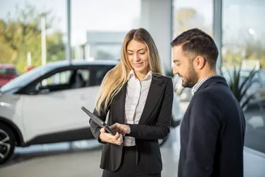 Car saleswoman showing to male customer car performance on tablet