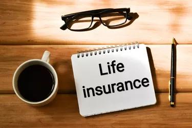 LIFE INSURANCE text written in a notepad near a cup coffee, eyeglasses and pen on a wooden background. Business concept. Flat lay.