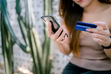 Beautiful smiling young Asian woman managing online banking with mobile app on smartphone and making mobile payment with credit card.