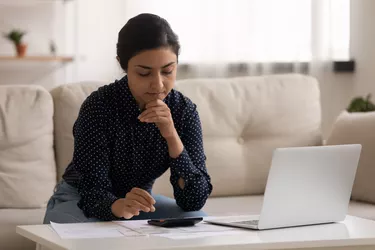 Thoughtful millennial indian woman sit on sofa calculate expenses