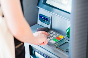 Person entering PIN code using ATM bank machine to withdraw money. Close-up.