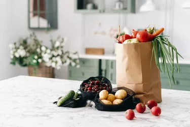 Various vegetables in paper grocery and black mesh bags on kitchen island