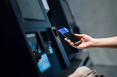 Close up of a young Asian woman using contactless payment via smartphone to pay for her shopping at self-checkout kiosk in a store