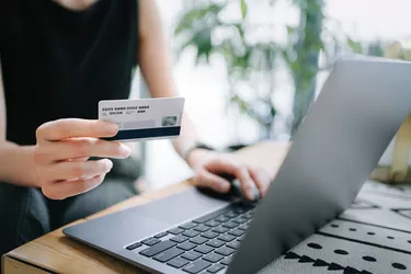 Close up of mid-section of young Asian woman relaxing in cafe, shopping online using laptop and making mobile payment with credit card on hand. Lifestyle and technology. Comfortable and fast online shopping experience