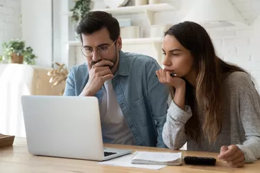 Couple with calculator and papers looking at computer screen.