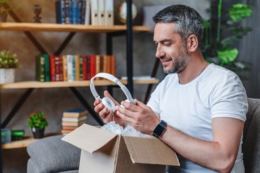 Joyful middle aged man receives his delivery with headphones at home