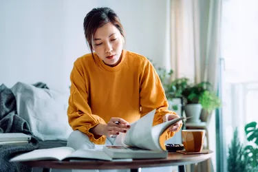 Focused young Asian woman reading book and making notes at home, concentrates on her studies. Further education concept