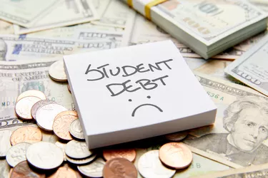 Student debt with sad face written on white sticky note on top of cash money with stack of money and coins