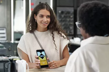 Elegant consumer in white knitted pullover showing coupon in smartphone to clerk