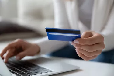 Closeup image female using laptop holding credit card